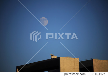 The moon rising above geometric buildings at dusk The moon rising above geometric buildings at dusk 133164424