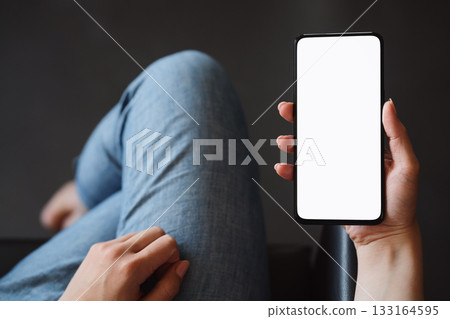 Young woman hold smarphone with white screen while sitting in a chair Young woman hold smarphone with white screen while sitting in a chair 133164595