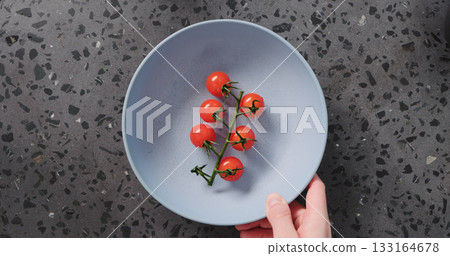 Top view man hand put cherry tomatoes in blue ceramic bowl on concrete background Top view man hand put cherry tomatoes in blue ceramic bowl on concrete background 133164678