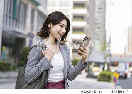 一位三十多歲的女商人正在城市裡看著她的智慧型手機螢幕。 一位三十多歲的女商人正在城市裡看著她的智慧型手機螢幕。 133166555