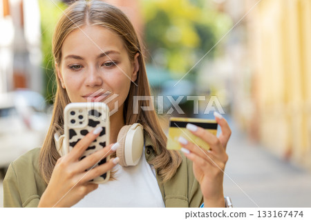 Caucasian woman using credit card and smartphone while transferring money, purchases online outdoors Caucasian woman using credit card and smartphone while transferring money, purchases online outdoors 133167474
