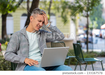 Mature man using laptop loses becoming surprised by sudden lottery results loss, fail in city street Mature man using laptop loses becoming surprised by sudden lottery results loss, fail in city street 133167578