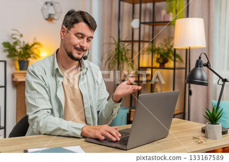 Young male customer service representative with headset using laptop computer at home office table Young male customer service representative with headset using laptop computer at home office table 133167589
