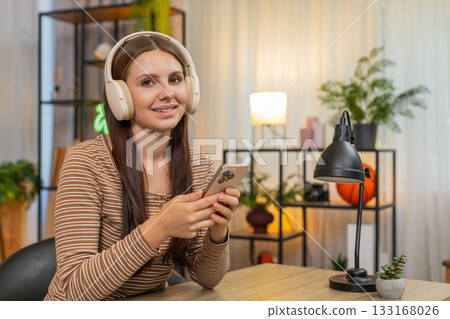 Young woman in headphones listens to work podcast saves ideas to notes on smartphone while focused 133168026