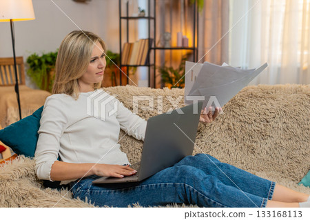 Adult woman frustrated with laptop work at home, throwing papers waving hand in irritation stress Adult woman frustrated with laptop work at home, throwing papers waving hand in irritation stress 133168113