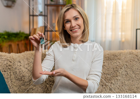 Adult woman celebrating new apartment at home, showing house keys proudly to camera with smile Adult woman celebrating new apartment at home, showing house keys proudly to camera with smile 133168114
