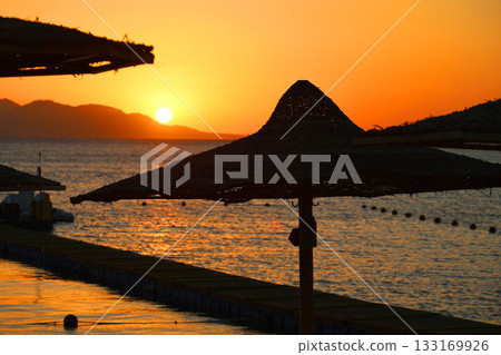 Sunrise over the sea against the backdrop of thatched umbrellas on the beach 133169926