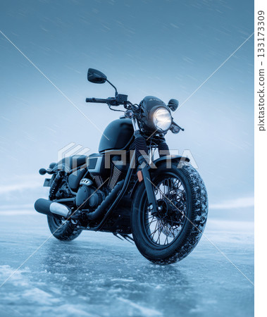 A black motorcycle stands on a frozen snowy surface as soft winter light falls around it A black motorcycle stands on a frozen snowy surface as soft winter light falls around it 133173309