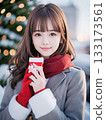 Smiling young woman holding a gift on a snowy night with sparkling Christmas lights 133173561