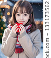 Smiling young woman holding a gift on a snowy night with sparkling Christmas lights 133173562