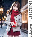 Smiling young woman holding a gift on a snowy night with sparkling Christmas lights 133173564