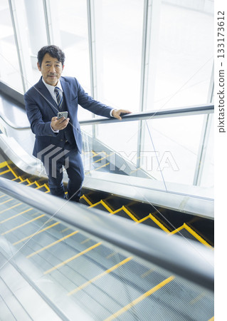 Businessman riding escalator 133173612