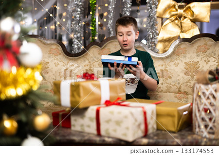 Happy joyful boy opening gift boxes during christmas celebration near new year tree 133174553