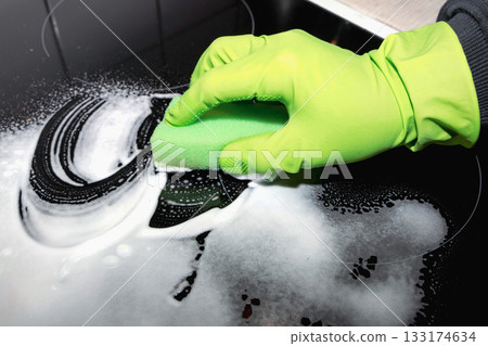 A man wearing cleaning gloves wipes the induction hob. A man wearing cleaning gloves wipes the induction hob. 133174634