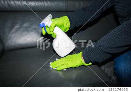 A man wearing cleaning gloves wipes the leather sofa. A man wearing cleaning gloves wipes the leather sofa. 133174635
