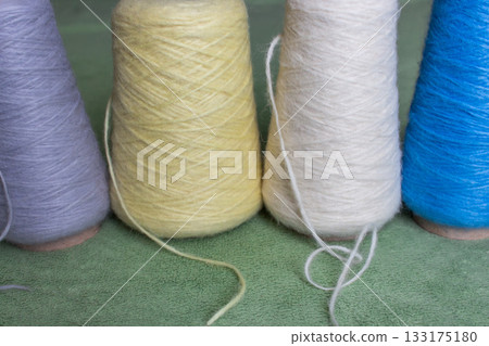 Variety colours of alpaca wool and silk. Cones of multicoloured yarn. Wool threads in a row. Row of blue, white, yellow and grey wool. Knitting hobby. Bobbins of yarn. Bright wool for knitting. Variety colours of alpaca wool and silk. Cones of multicoloured yarn. Wool threads in a row. Row of blue, white, yellow and grey wool. Knitting hobby. Bobbins of yarn. Bright wool for knitting. 133175180