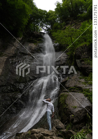 A man looks at a waterfall in the mountains in surprise. Waterfall in Georgia 133175791