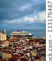 Large cruise ship moored in historic center of Lisbon, Portugal. Alfama area full of original buildings with red-tiled rooftops, high church bell tower, cloudy sky at afternoon. Travel destination 133176487