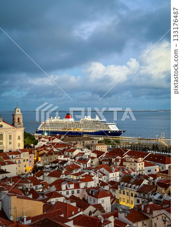 Large cruise ship moored in historic center of Lisbon, Portugal. Alfama area full of original buildings with red-tiled rooftops, high church bell tower, cloudy sky at afternoon. Travel destination Large cruise ship moored in historic center of Lisbon, Portugal. Alfama area full of original buildings with red-tiled rooftops, high church bell tower, cloudy sky at afternoon. Travel destination 133176487