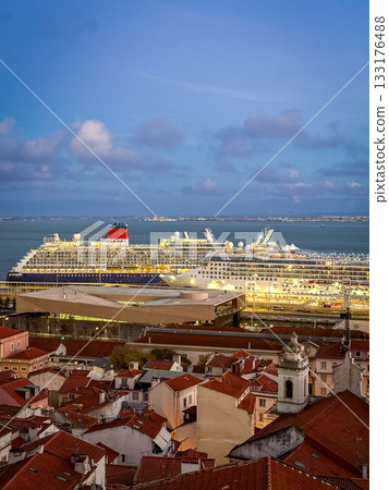 Two large cruise ship manoeuvre by terminal pier near historic center of Lisbon, Portugal. Alfama area, original buildings with red-tiled rooftops, cloudy sky at afternoon. Travel destination, voyage 133176488