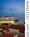 One large cruise ship leaving port of Lisbon, Portugal, another cruse liner moored by historic area of Alfama with original buildings with red-tiled rooftops, at night. Travel destination, voyage 133176490