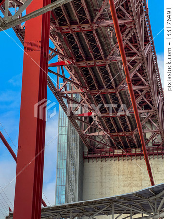 Upshot view of tower beam, main girder and anchorage block of famous red April 25th or 25 de Abril bridge in Lisbon, Portugal, blue sky, white clouds on sunny day. Tourist attraction, travel Upshot view of tower beam, main girder and anchorage block of famous red April 25th or 25 de Abril bridge in Lisbon, Portugal, blue sky, white clouds on sunny day. Tourist attraction, travel 133176491