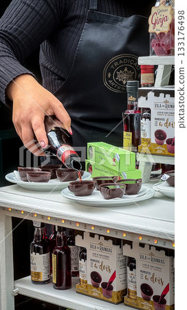 Obidos, Portugal - Dec 30, 2023: Female hand pouring traditional Portuguese ginja liqueur into edible chocolate cups, sweet cherry drink, popular local specialty and tourist souvenir. Authentic 133176498