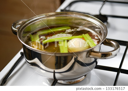 Cooking an aromatic vegetable broth with celery and onion in a stainless steel pot on the stove Cooking an aromatic vegetable broth with celery and onion in a stainless steel pot on the stove 133176517