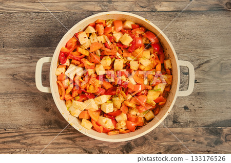 Colorful vegetable medley being prepared in a large pot on a wooden surface 133176526