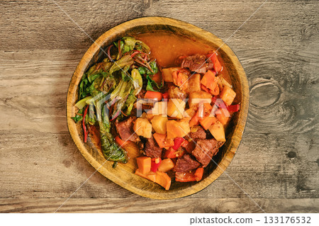 Hearty beef stew served with greens and vegetables in a rustic wooden bowl Hearty beef stew served with greens and vegetables in a rustic wooden bowl 133176532