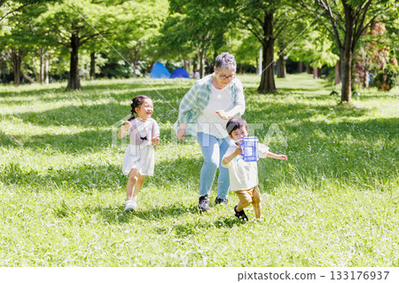 Grandma playing with her grandchildren in a park with fresh greenery Grandma playing with her grandchildren in a park with fresh greenery 133176937