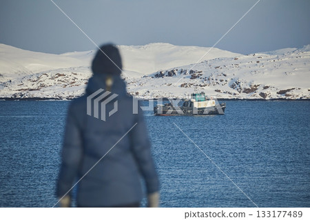 A girl in a blue jacket against the background of a non-freezing sea and a ship in winter, blurry focus, visible on the silhouette 133177489