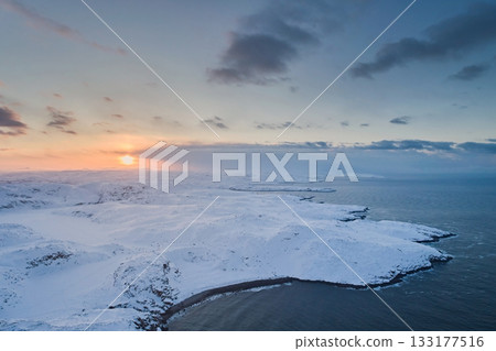 Aerial view of the non-freezing Barents Sea on the Kola Peninsula in winter against the sunset sky and the sun 133177516
