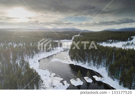 Aerial view landscape: ice-free river and snowy forest against a bright sunny sky in winter Aerial view landscape: ice-free river and snowy forest against a bright sunny sky in winter 133177520