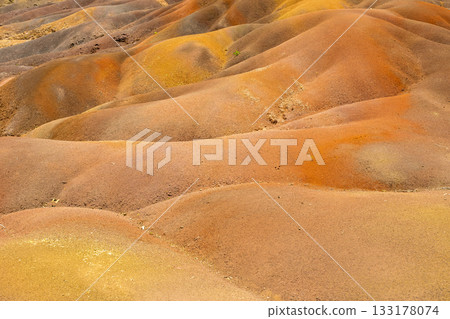 Close view of Chamarel Seven Coloured Earth rippled dunes with warm tones, soft curves, and fine granular texture Close view of Chamarel Seven Coloured Earth rippled dunes with warm tones, soft curves, and fine granular texture 133178074