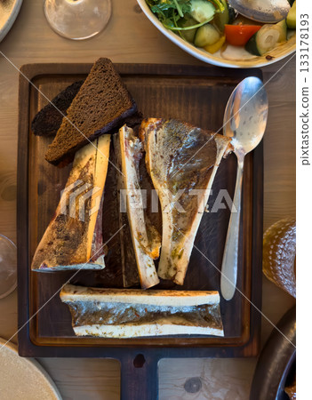 Traditional bone marrow appetizer served on wooden board with dark rye bread and vegetable salad Traditional bone marrow appetizer served on wooden board with dark rye bread and vegetable salad 133178193