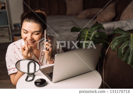 Woman applying lip liner while talking on smartphone 133178718