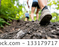 Woman wearing hiking boot ascends muddy path in outdoor summer green scenery. 133179717