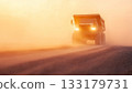 Dusty dump truck driving on dirt road at sunset. 133179731
