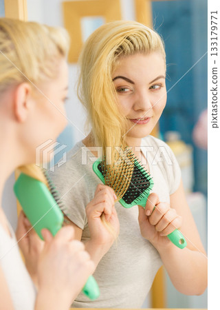 Woman brushing her blonde hair in bathroom 133179771