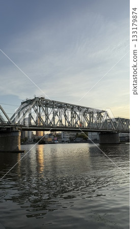 City bridge over calm river at sunset reflecting in water with an urban skyline in background 133179874