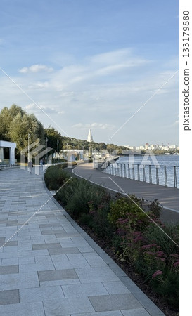 Riverside promenade with walkway, railings, and scenic view under blue sky background Riverside promenade with walkway, railings, and scenic view under blue sky background 133179880