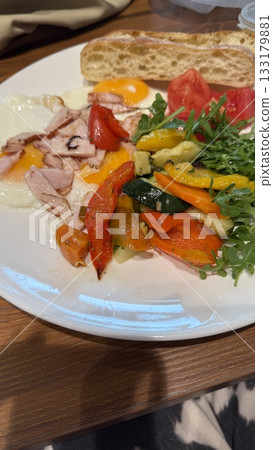 Breakfast plate with fried eggs, bacon, grilled vegetables, tomato, arugula, and bread Breakfast plate with fried eggs, bacon, grilled vegetables, tomato, arugula, and bread 133179881