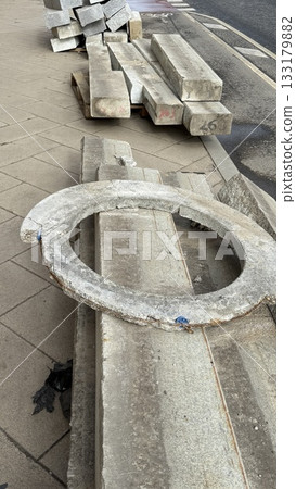 Concrete construction materials stacked on pavement, including circular and rectangular slabs Concrete construction materials stacked on pavement, including circular and rectangular slabs 133179882