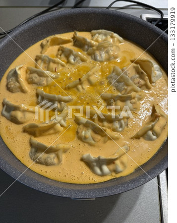 Dumplings cooking in a pan with rich sauce, overhead view showing delicious meal preparation Dumplings cooking in a pan with rich sauce, overhead view showing delicious meal preparation 133179919