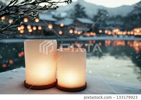 Soft glowing lantern on snowy lakeside with warm reflections and distant village lights, peaceful winter festival atmosphere 133179923