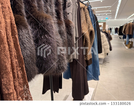 A row of warm autumn and winter clothing, including faux fur, knits, and textures, hangs neatly in a store A row of warm autumn and winter clothing, including faux fur, knits, and textures, hangs neatly in a store 133180026