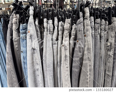 A tightly packed row of jeans in different shades of blue and gray hangs in a casual fashion store A tightly packed row of jeans in different shades of blue and gray hangs in a casual fashion store 133180027
