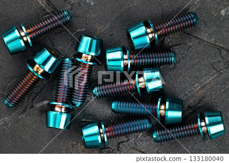 Screws made of blue-purple anodized titanium alloy on a black textured background Screws made of blue-purple anodized titanium alloy on a black textured background 133180040