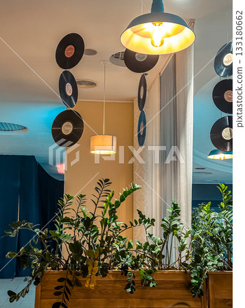 Interior design featuring hanging vinyl records and stylish pendant lights, creating a vibrant atmosphere with greenery and modern decor elements Interior design featuring hanging vinyl records and stylish pendant lights, creating a vibrant atmosphere with greenery and modern decor elements 133180662